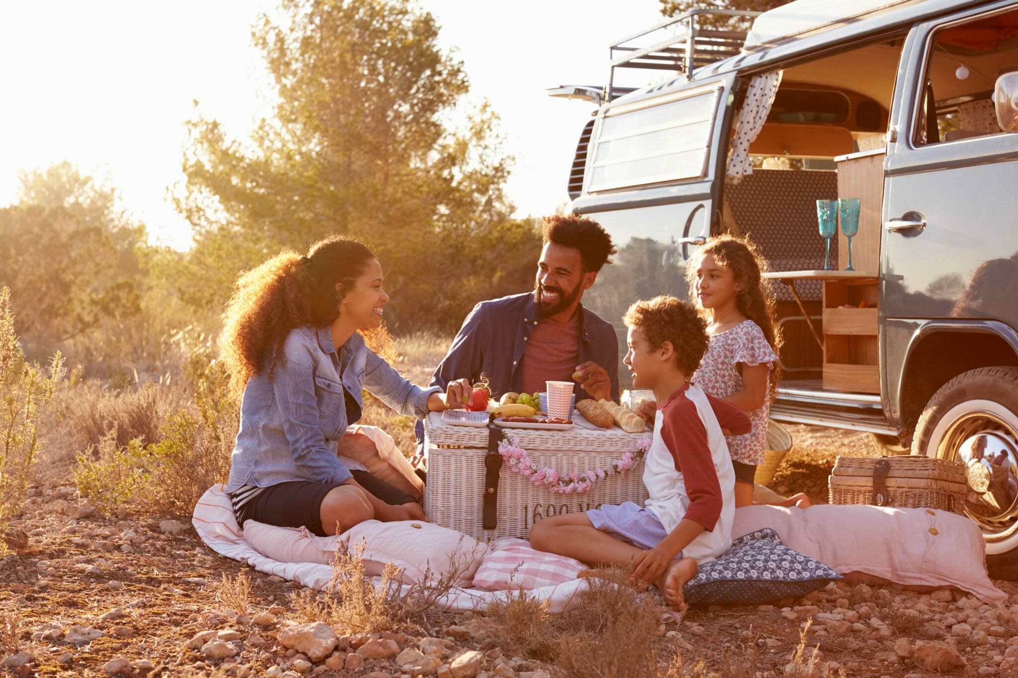 Familie, die auf dem Boden neben ihrem Wohnmobil picknickt.