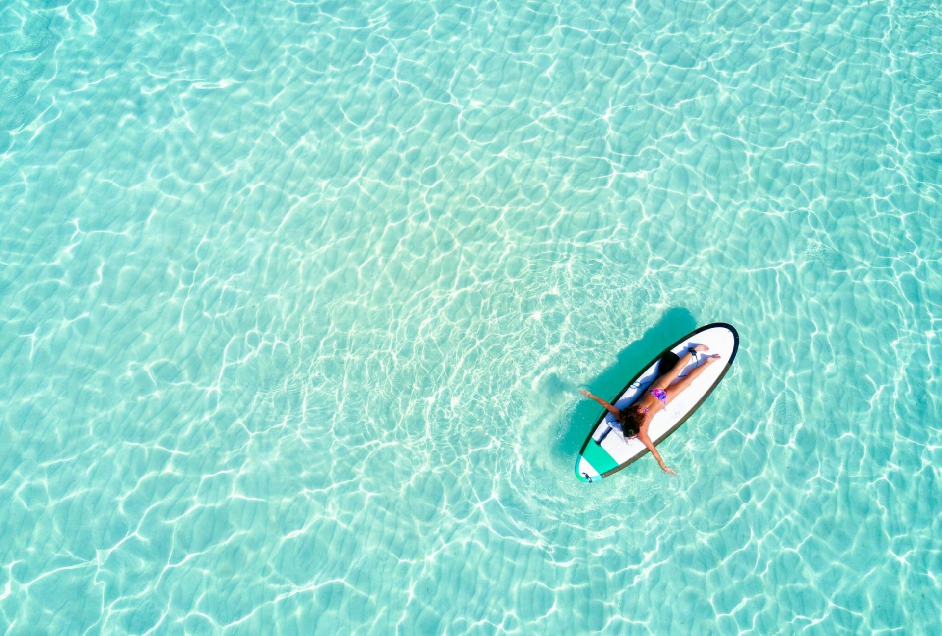 Person auf einem Surfbrett in einem klaren blauen Meer.